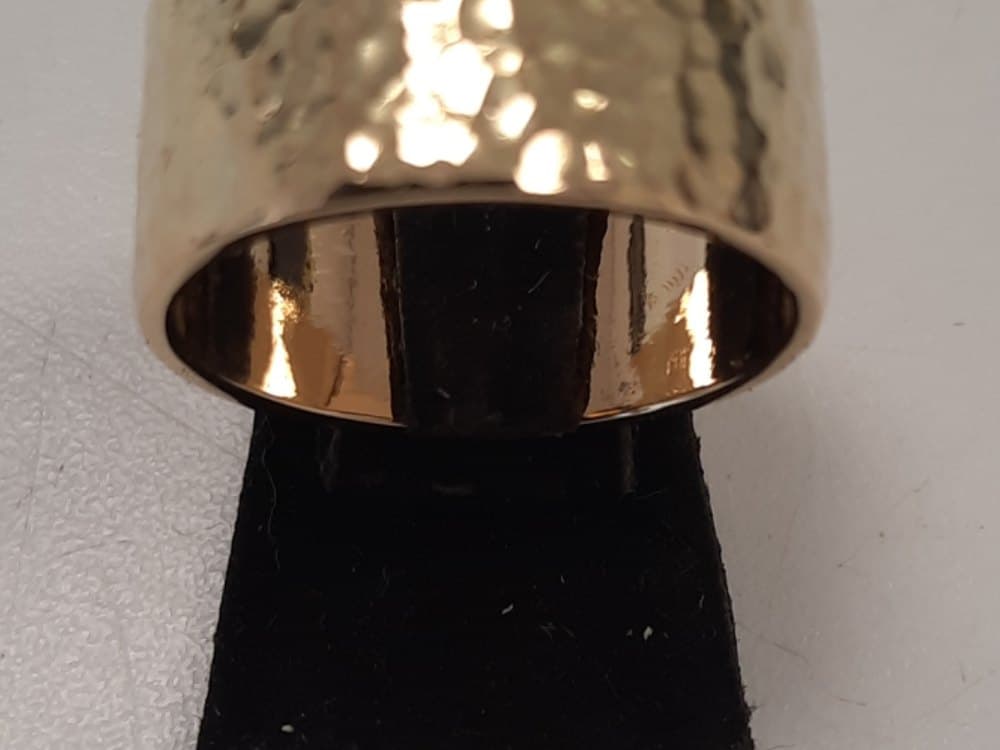 Brede gouden ring met een hamerslagpatroon, op een zwart standaardje