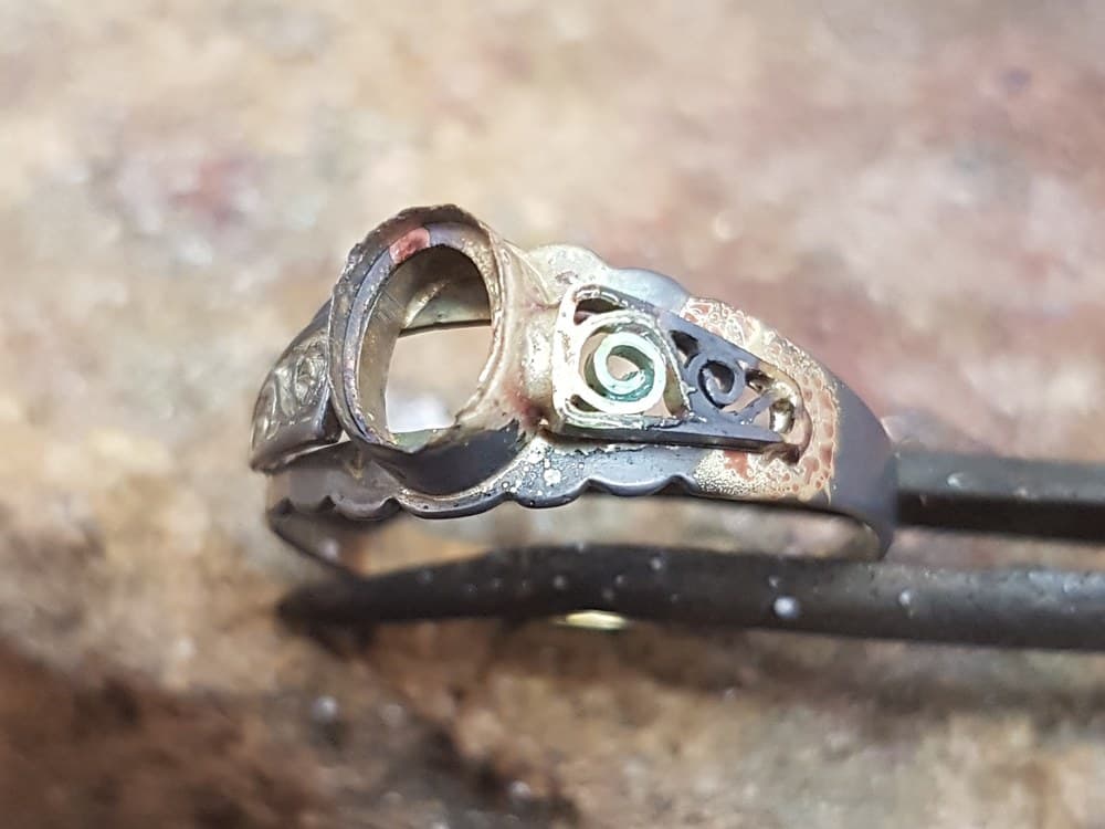De ring in de soldeertang, zwartgeblakerd van de brander, met het nieuwe zijstuk erin gesoldeerd