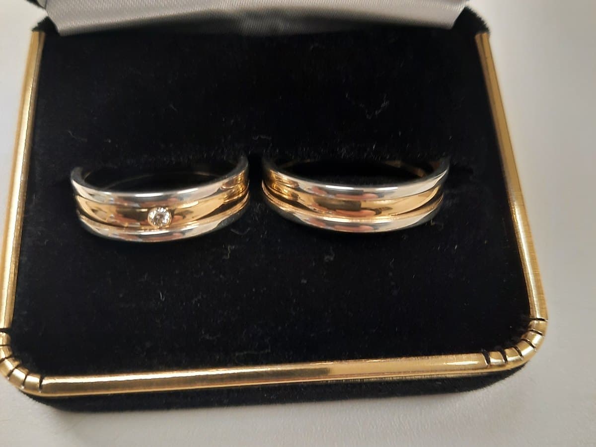 Twee trouwringen van wit- en roodgoud, met een diamant, in een geopend ringdoosje