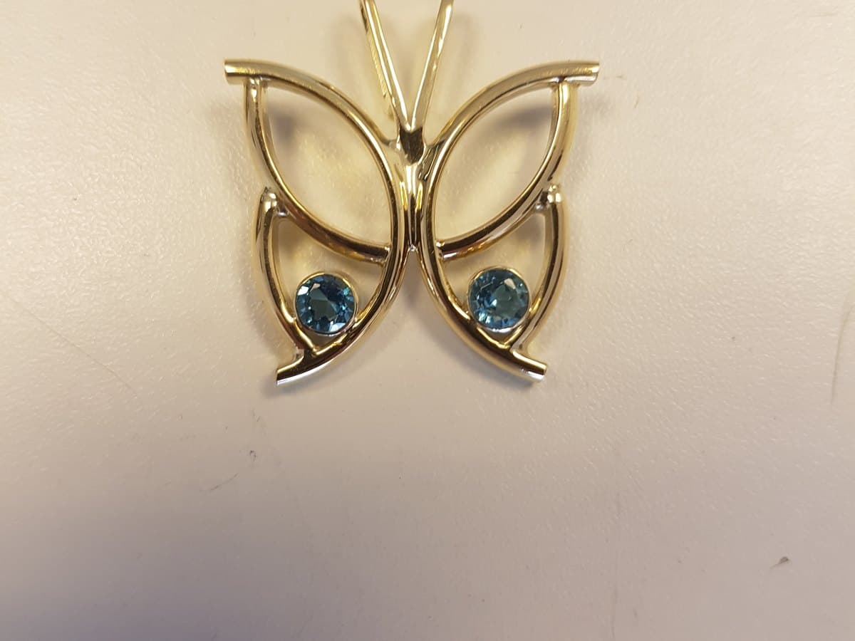 Gouden hanger in de vorm van een vlinder, met in elke vleugel een blauwe topaas